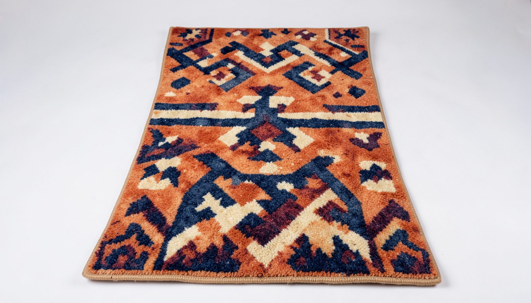 A hand-felted wool rug with geometric Mesopotamian-inspired motifs in warm terracotta, sand and deep navy tones